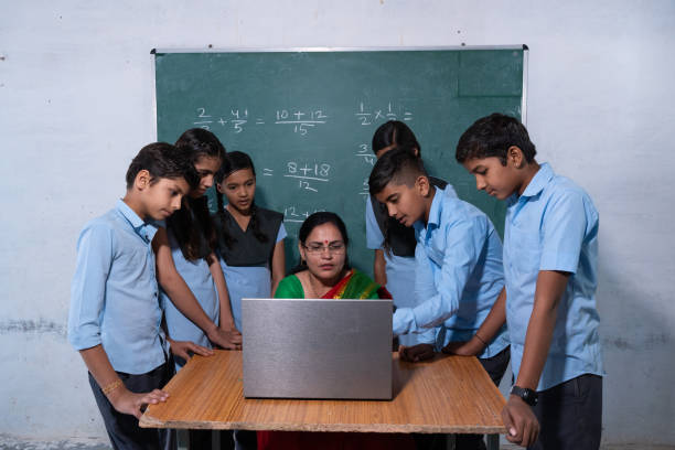 indian female teacher using laptop in her classroom to make children easier to understand, learn. Group of school kids in uniform looking at laptop screen. Education concept.