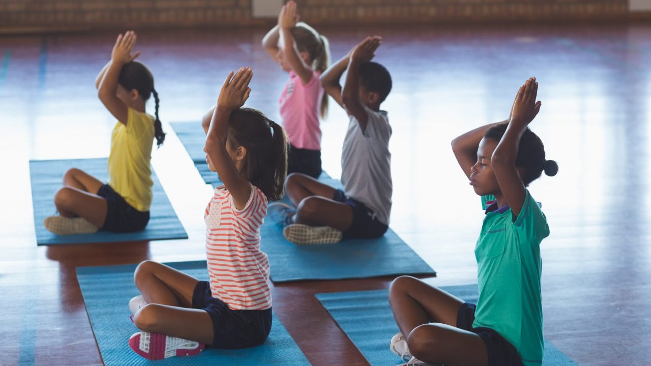 School kids meditating during yoga class in basketball court at school gym